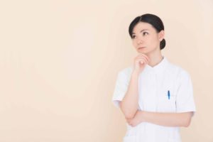 薄オレンジの背景前で悩んでいる女性