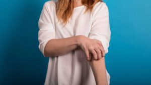 白い服を着た女性が腕を掻いている