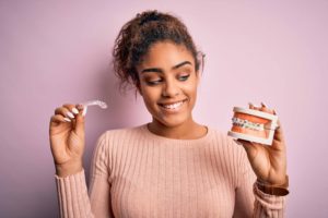 ピンクのニットを着た女性がマウスピースとワイヤー矯正が付いた歯の模型を持っている