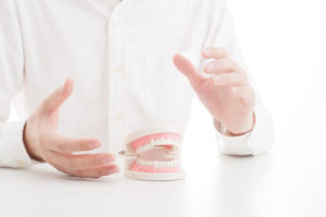 白いシャツを着た人の前に歯の模型がある