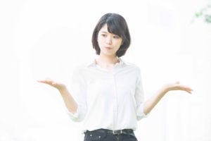 両手で比較するポーズをしている白いブラウスを着た女性