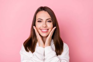 ピンクの背景の前で両手を頬に当てている女性