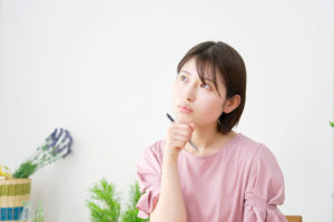ピンクの服を着た女性がペンを持ち悩んでいる