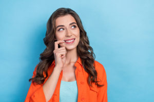 オレンジのシャツを着た女性が右上を見て口を指差している