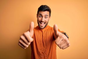 オレンジ背景の前て両手でグッドサインを出している男性