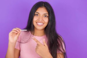 紫の背景の前で片手にマウスピースを持っている女性がいる