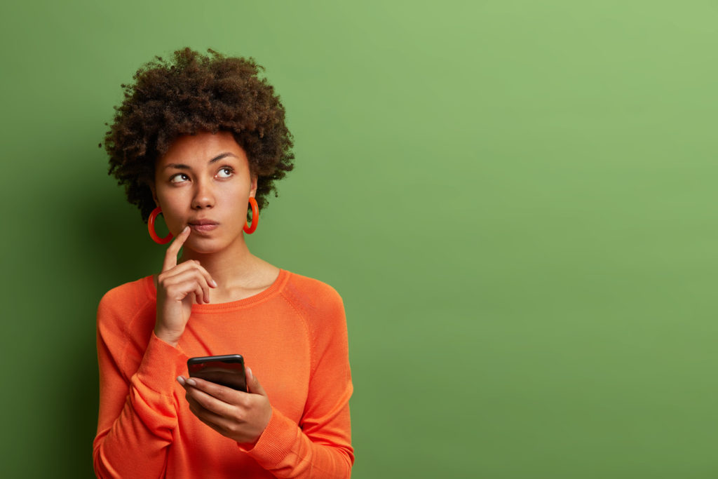 緑の背景の前でスマホを持って考える女性